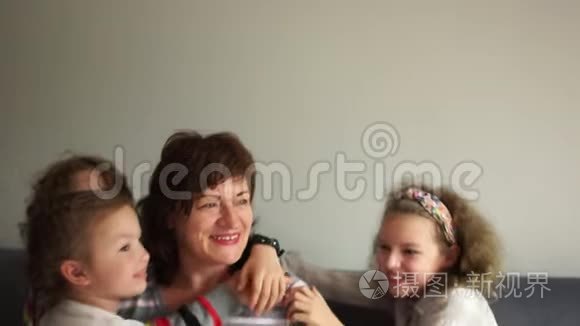 可爱的好祖母和她的四个孙子孙女坐在沙发上拥抱。 带着女保姆