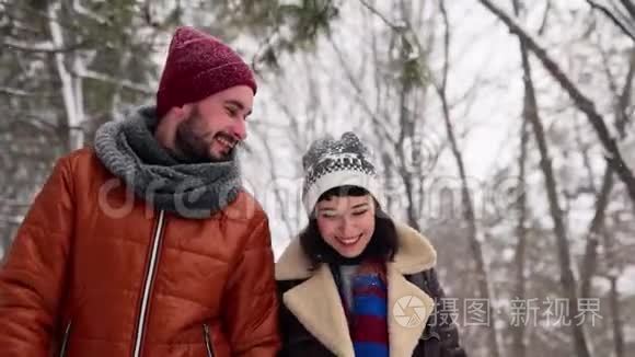 一对相爱的年轻夫妇在下雪的时候在公园里散步。男人和女友手牵手在冬日赏雪