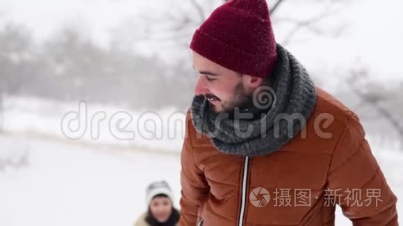 可爱的夫妇在下雪的冬天滑雪。 下雪时，男人和女朋友拉雪橇。 女人玩得开心