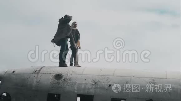 一对年轻的旅行夫妇站在冰岛坠毁的DC3飞机上，在大风天一起举手。