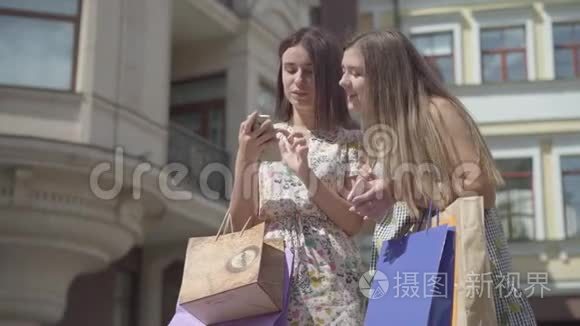 两个可爱的女朋友购物后，带着购物袋在户外手机上自拍。 快乐女孩的休闲