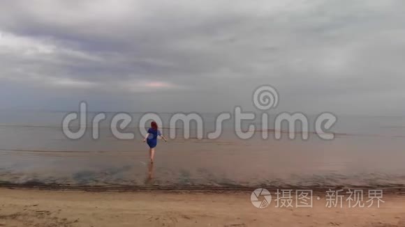 空中：年轻女子穿着蓝色鲜艳的裙子跑步-浅水风景，波罗的海的黄色日落景观-