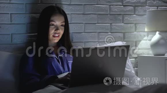 快乐的女人晚上在笔记本电脑上完成项目，躺在床上，加班