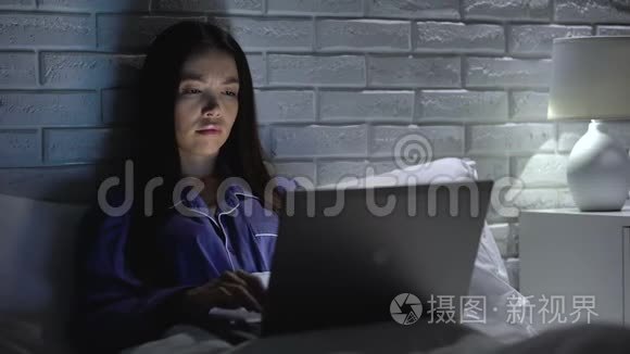 睡眠不足的女人晚上在床上用笔记本电脑工作，在无聊的项目中没有动力