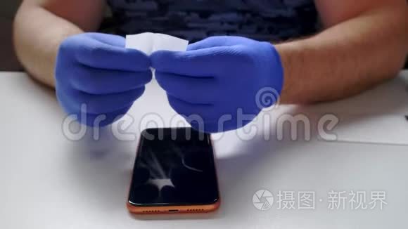男性手中的蓝色手套取代了一个破碎的钢化玻璃屏幕保护器的智能手机。 一个男人准备智能手机