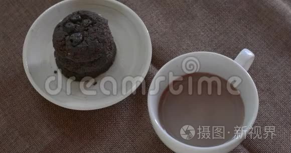 喝热巧克力在白色陶瓷杯与模糊的黑巧克力饼干棕色桌布。 为每个人提供美味的饮料