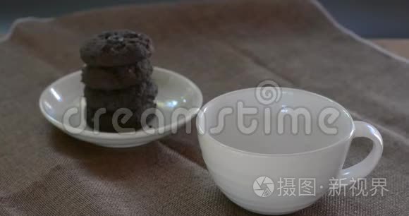 将热巧克力倒入棕色桌布上的白色陶瓷杯和模糊的dakr巧克力蛋糕上。 为每个人提供美味的饮料