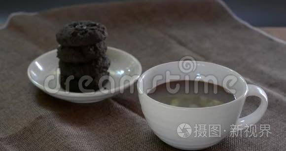 喝热巧克力在白色陶瓷杯与模糊的黑巧克力饼干棕色桌布。 为每个人提供美味的饮料