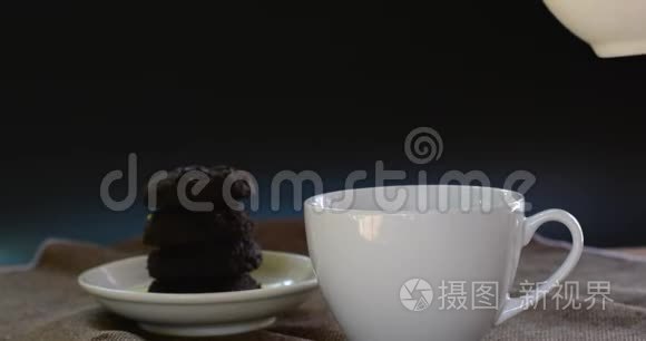 将热巧克力倒入棕色桌布上的白色陶瓷杯和模糊的dakr巧克力蛋糕上。 为每个人提供美味的饮料