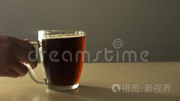 男性手移动全马克杯深色啤酒在桌子上特写，凝结纹理4K。