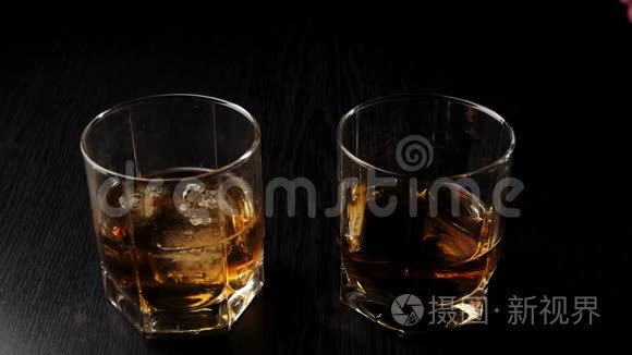 豪华威士忌。 手把冰扔到一个玻璃杯里，在黑桌上，靠近玻璃杯，有威士忌和冰。 苏格兰威士忌。