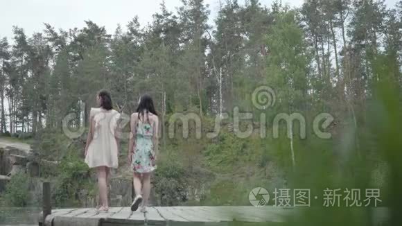两个可爱的年轻女人穿着夏装站在岩石的顶部，看着大自然。 漂亮的女孩走出去