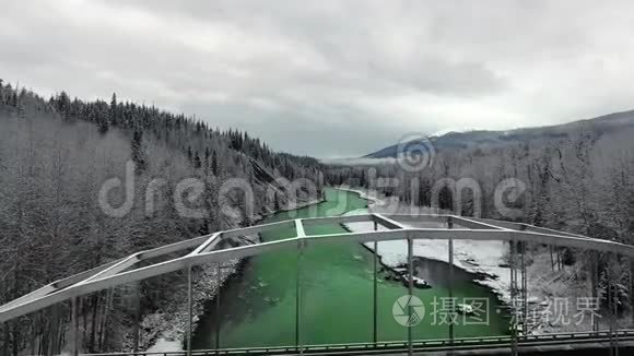 空中照相机在茂密的冬季松林中穿过一座桥，可以看到山景