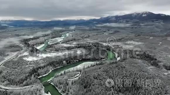 一架正在一片茂密的松林一条河流和一条高速公路上旋转，以观察冬天蓝雪覆盖的山脉