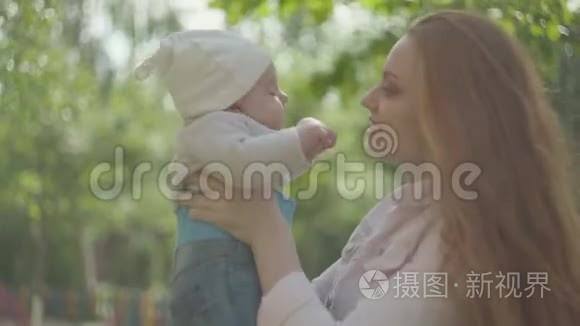 年轻美丽的红头发母亲抱着她可爱的孩子在她的怀里亲吻，在春天阳光明媚的日子里和他说话