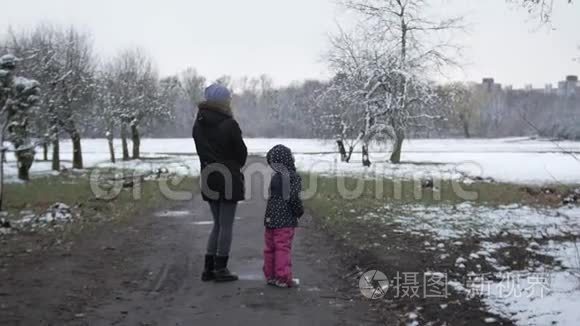 妈妈带着一个女儿在春天多云的公园里散步，下雪了