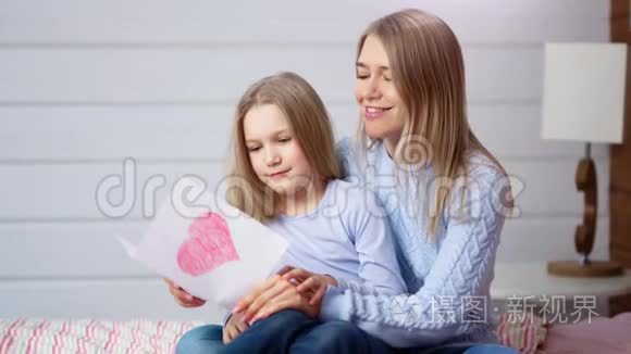 快乐的妈妈和可爱的小女儿捧着红色的明信片庆祝快乐的妈妈一天