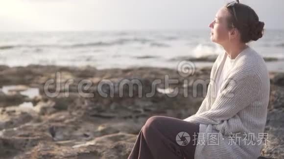 年轻时尚的女人坐在岩石海岸上视频