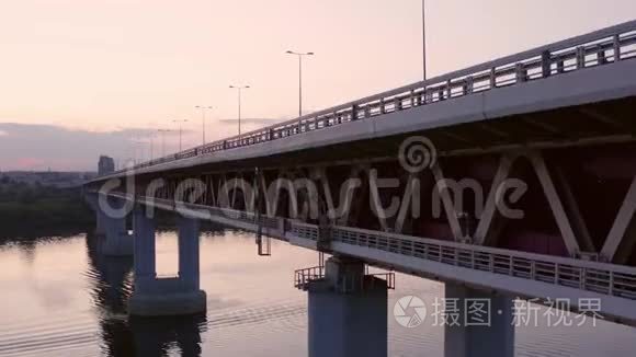 汽车在城市河流的桥上行驶。 无人机在日落背景下观看桥上的汽车交通。 城市建筑景观