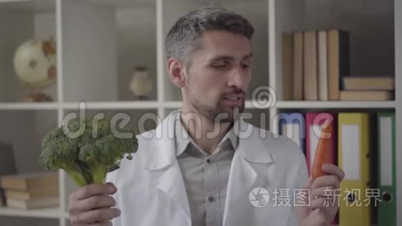 一幅穿着白色长袍的英俊男子在镜头中提出胡萝卜和西兰花的肖像。 现代熟练的医生