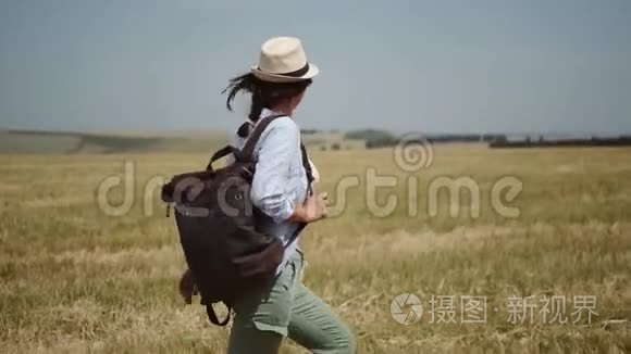 年轻的女旅行者带着背包走过田野