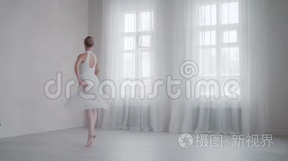 芭蕾舞演员踮起脚尖，穿着雪白的连衣裙，在大窗户的背景下，在明亮的工作室里旋转着