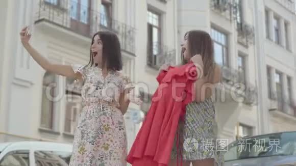 两个快乐的女朋友购物后，带着购物袋，在手机上自拍，户外穿着新衣服。 休闲