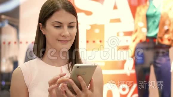 慢动作年轻女子坐在购物中心微笑。 用她的智能手机和朋友聊天