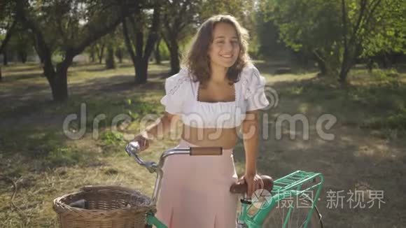 有魅力的年轻女人的肖像，卷发，骑着自行车站在花园或公园里。 农村生活。 复古