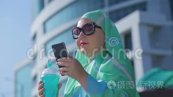 一位年轻的穆斯林妇女，戴着浅色围巾和太阳镜，戴着现代建筑的背景