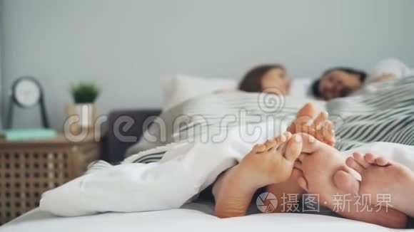 男人和女人的双脚接触床上的情侣躺在毯子下面谈话
