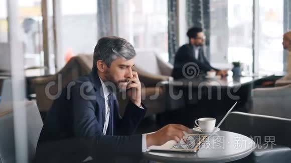 中年人用智能手机打电话，在咖啡馆里用笔记本电脑
