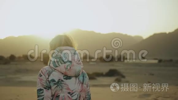 美丽的金发女人在沙漠中日落时散步。 女性穿越沙漠，沙丘，特写，慢动作，4k