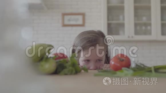 肖像可爱可爱的小女孩从桌子上看，躲在镜头里。 新鲜蔬菜西葫芦