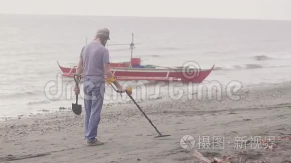 戴着耳机的人正在海滩上工作，手持探测器在日出时在海岸线上的沙滩上发现贵重物品。