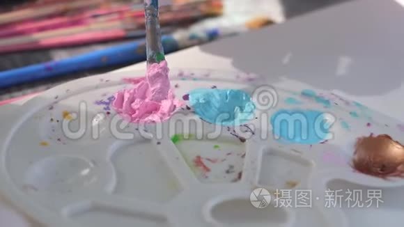 女艺术家用画笔在调色板上混合粉红色的颜料。