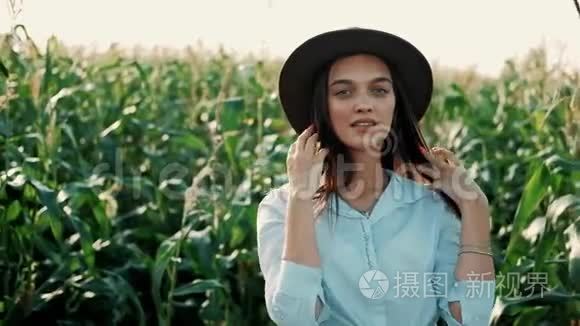 戴着帽子的美丽少女站在玉米地边微笑，在夕阳下看镜头的画像