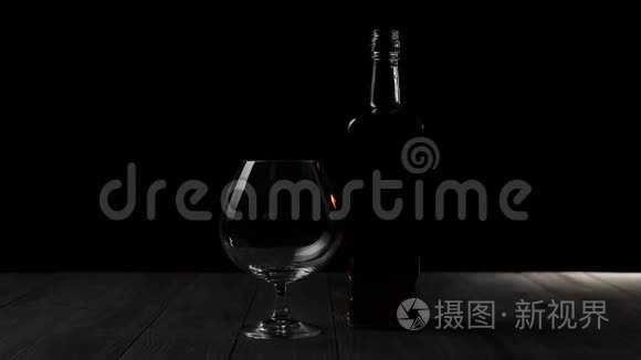 豪华白兰地。 一个方形瓶子里的金色干邑站在黑色背景的木桌上的玻璃旁边。