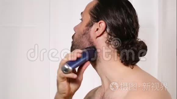 英俊的年轻人留着长发，在浴室里用修剪器刮胡子。 光线优美，背景模糊..