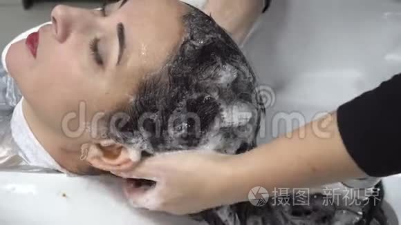 特写镜头，发型师用白色脸盆在一家发廊里给一位东方女性的头发梳洗。 头发护理。 4K