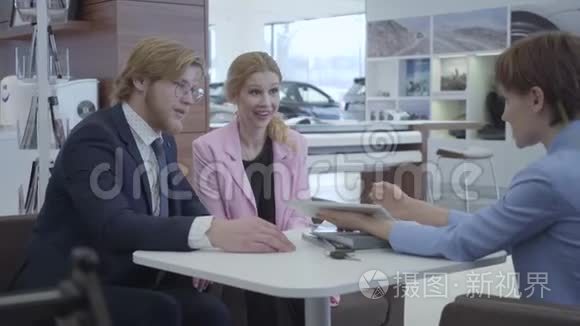 一位穿着时尚西装的汽车销售人员向年轻成功的夫妇提供了在平板电脑上选择汽车品牌的机会。 汽车