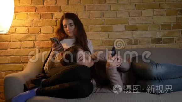 年轻的高加索女孩在沙发上放松，在舒适的家庭氛围中观看他们的智能手机的肖像。