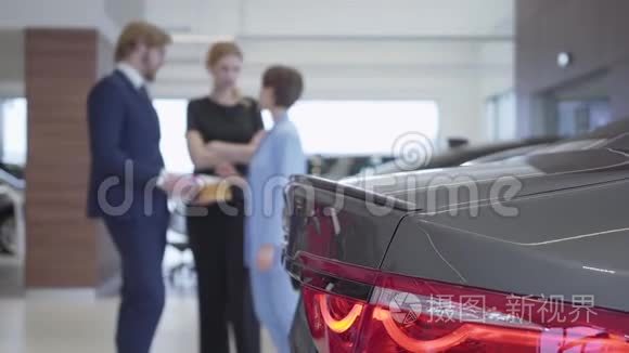 在现代汽车车展的背景下，推销员和两位女客户的模糊数字在交谈。 女人选择