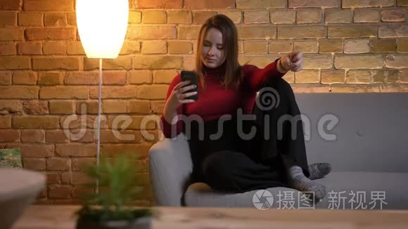 年轻漂亮的白种人女性坐在舒适的沙发上放松时在手机上发短信的特写镜头