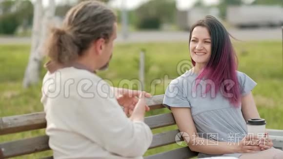 一位轻松迷人的中年男子，长发灰白，一位染发的年轻女子坐在公园的长凳上。