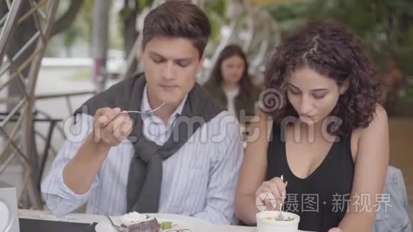 一对幸福夫妇坐在户外咖啡馆吃蛋糕的肖像。 年轻人和女人一起享受他们的晚餐。 这就是
