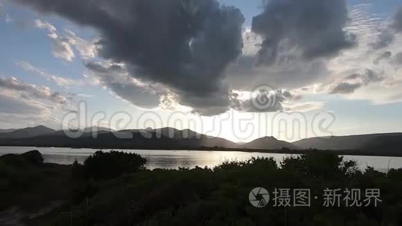 夕阳西下，一片海洋泻湖上一片戏剧性的天空的全景，地平线上群山的黑色轮廓