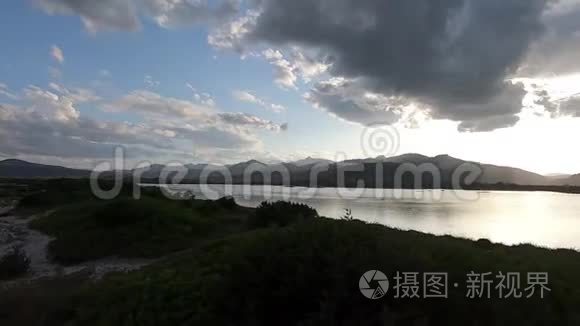 夕阳西下，一片海洋泻湖上一片戏剧性的天空的全景，地平线上群山的黑色轮廓