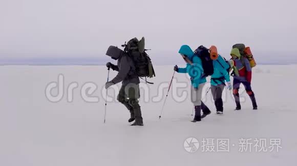 一群活跃的男人和女人带着背包和滑雪杆在强烈的冬季风中穿过冰冻的河流。