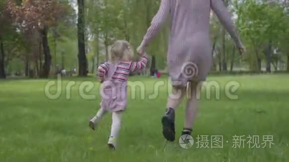 妈妈和小女儿牵着手在神奇的绿色公园里跑来跑去。 在公园里玩耍的女人和小孩